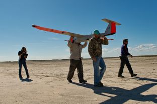 Micheal Cincienne of Absolute Aerospace and Texas A&M Corpus Christi, engineering student Adam Ersepke, and lab coordinator Jack Edward Esparza carry the University’s RS-16 unmanned aerial vehicle, otherwise known as a drone, back to the command center after a test flight over the Kennedy Ranch near Sarita, Texas on January 18, 2013.