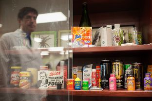 Recalled products, natural threats, choking hazards, and items that could cause emergencies when large amounts are ingested by children, are displayed at the South Texas Poison Center in San Antonio. Miguel Fernández, managing director of the center, is reflected in the display case glass.