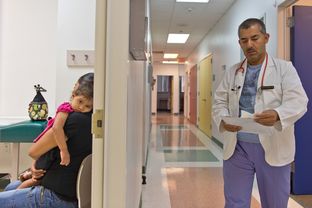 Yesenia Alvarado holds her daughter, Medicaid patient Melanie Almaraz, 2, while waiting to see Dr. Alberto Vasquez for treatment of a fever at the Su Clinica Familiar in Harlingen, Texas on Jul. 9, 2013.