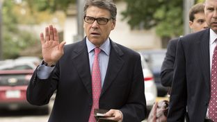 Gov. Rick Perry holds his Texas driver's license and his wallet as he heads to a west Austin early voting site on October 30, 2013.