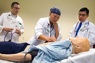 Third-year medical student Summer Scavone (middle) tries to listen to the SimMan's lungs for wheezing.