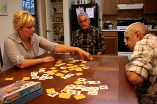 Health care assistant Crystal Kreig plays a card game with Steve Parker (center) and Eulalio Alvarada (right) at a group home operated by D&S Residential, Inc. Companies like D&S used to handle case management for their clients, but a budget change sent that responsibility to local Mental Retardation Authorities.