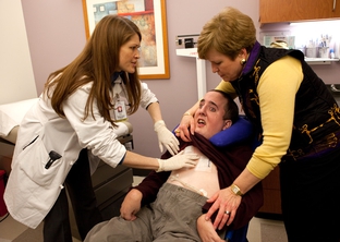 Dr. Tamiko Kido checks out Benjamin Ligums' sutures at Baylor's Transition Medicine Clinic in Houston, as his mother, Ann Ligums, looks on. Ben was given 18 months to live when he was born with a degenerative brain disease. He's now 26.