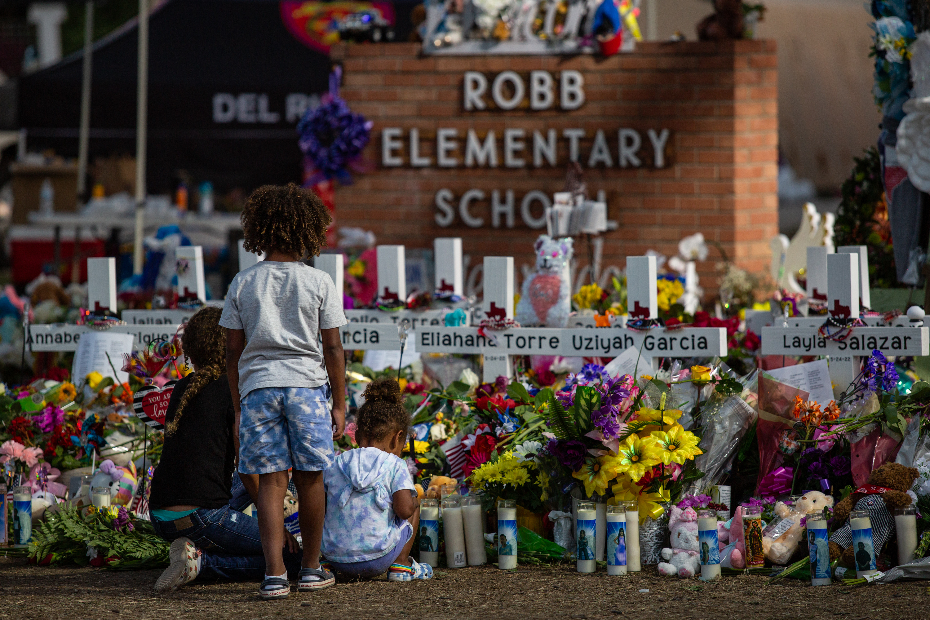 Hundreds wait in line holding flowers and each other to pay their respects at a memorial in front of the Robb Elementary School on Saturday evening.