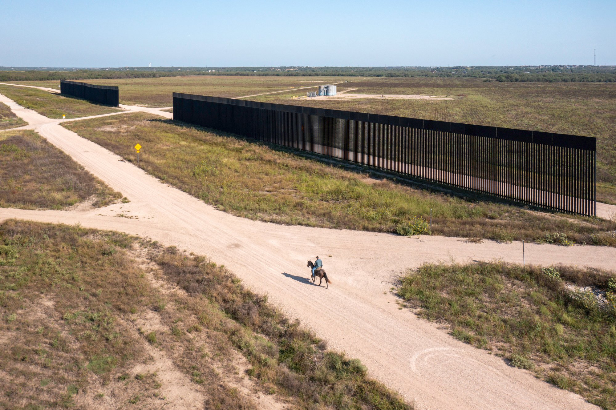 A person rides a horse down a dirt road, where two incomplete sections of border wall.