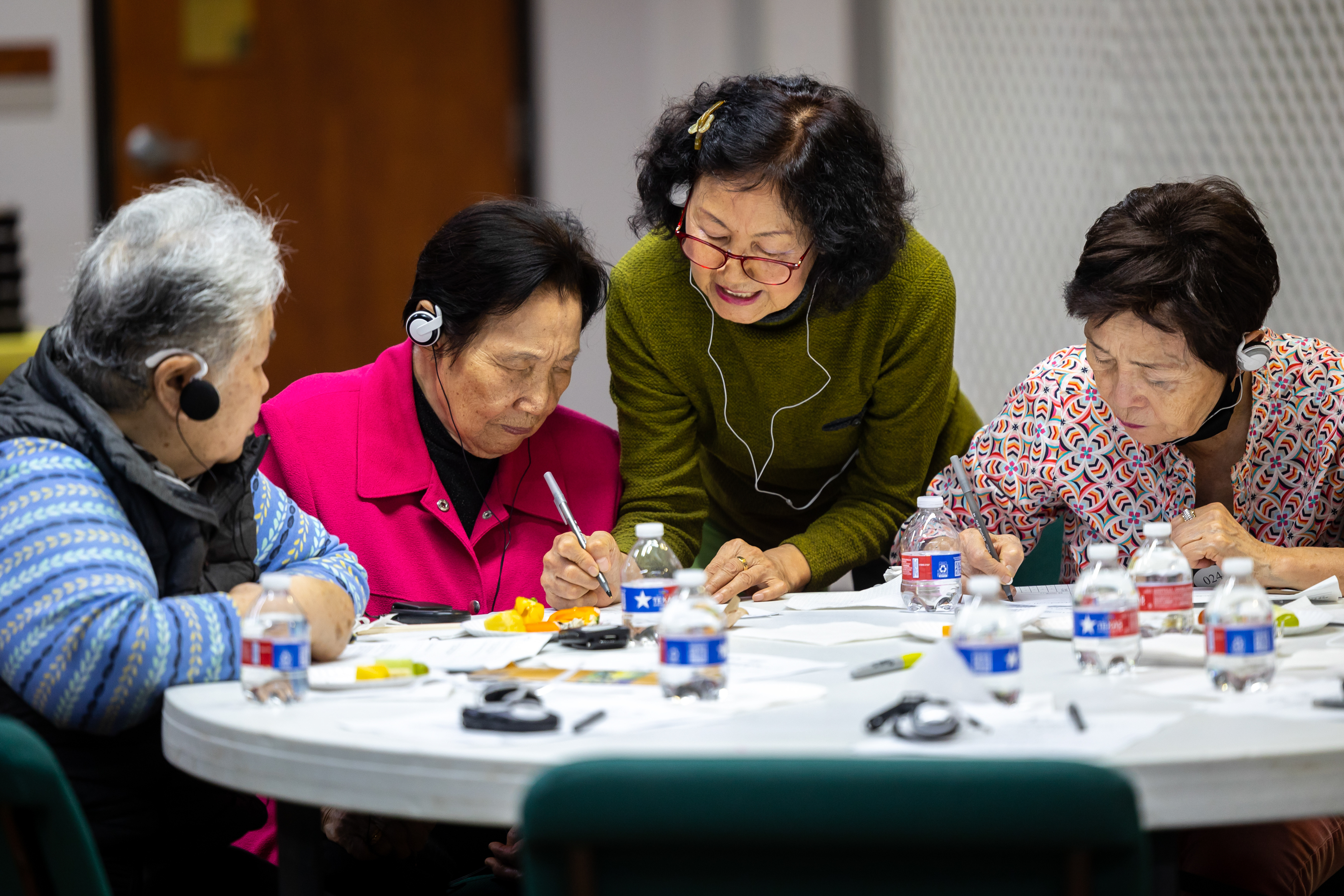 Group of three Korean Americans at a table with one person writing and talking.