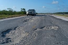 A driver maneuvers around a badly damaged portion of the IH 37 frontage road south of FM 99 in Live Oak County, TX on Firday, August 16, 2013