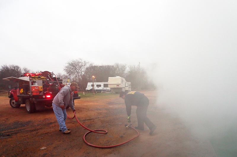 Part time senior fire fighter Richard Prado responds to a radio call about a dumpster fire at Pat's RV Park on Main St in Cotulla, a man camp that houses oil field workers, during his 24 hour shift at the La Salle County Fire Department, Thursday, January 23, 2014. Park owner Pat Niaves assists him with the hose since he is working the shift alone.